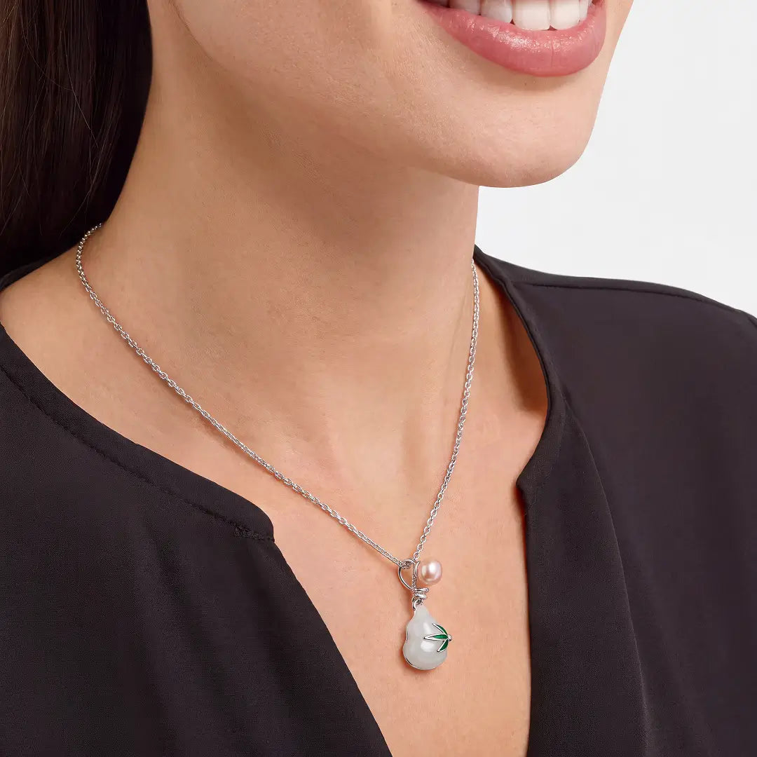 A close-up of a woman wearing a silver chain necklace with a unique pendant. The pendant features a small pink pearl and a larger irregular white pearl with a small green leaf inlay, set in a silver setting.