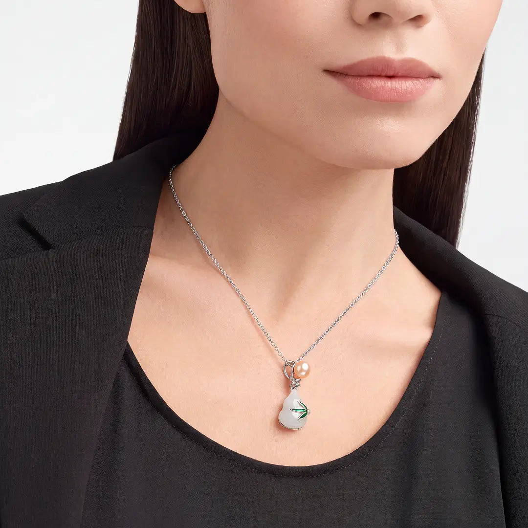 A close-up of a model wearing a delicate silver chain necklace with a pear-shaped pendant. The pendant features a white mother-of-pearl inlay with a green leaf design and a small pearl accent at the top.