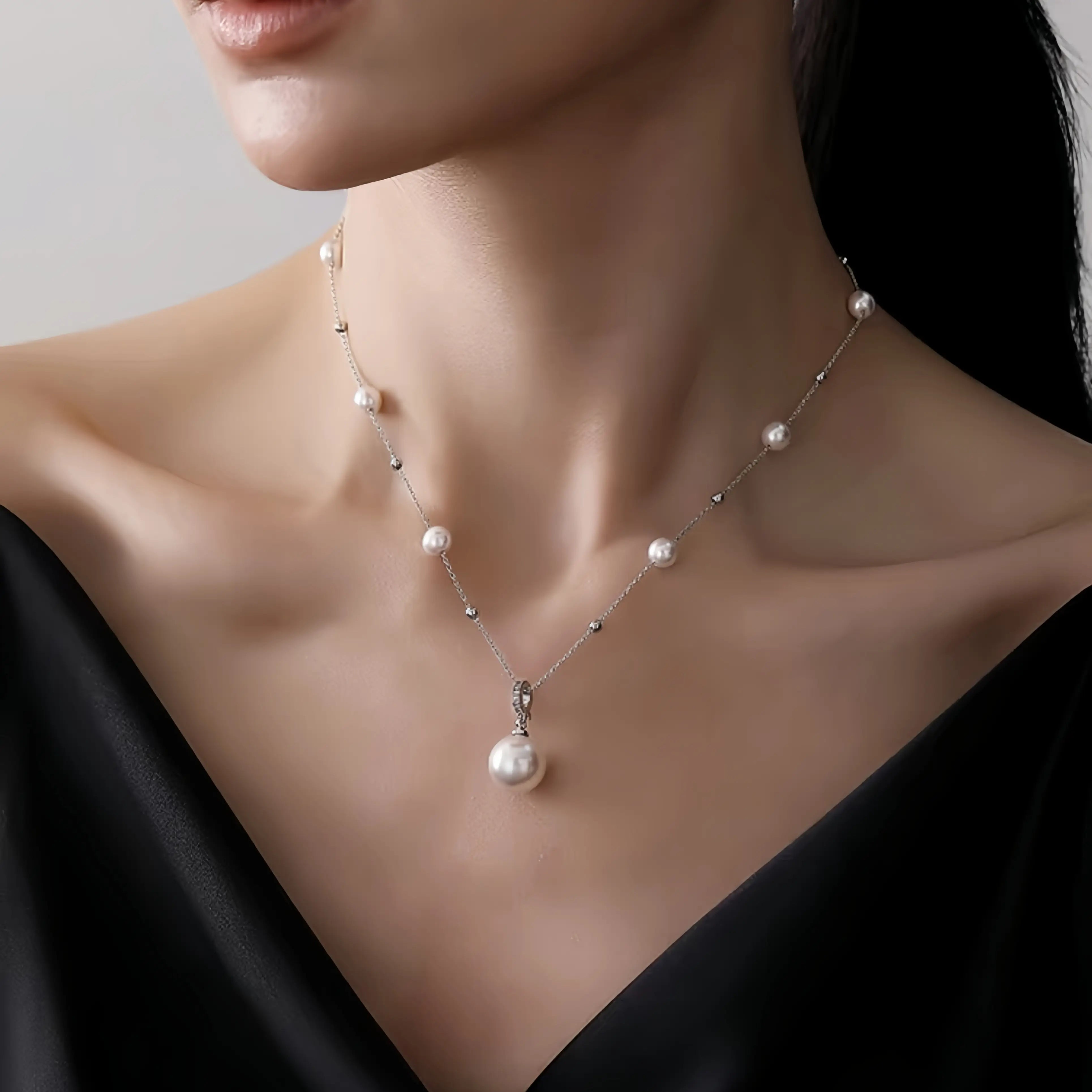 A close-up of a model wearing a delicate silver chain necklace with small white pearls spaced along the chain and a larger pearl pendant hanging at the center.