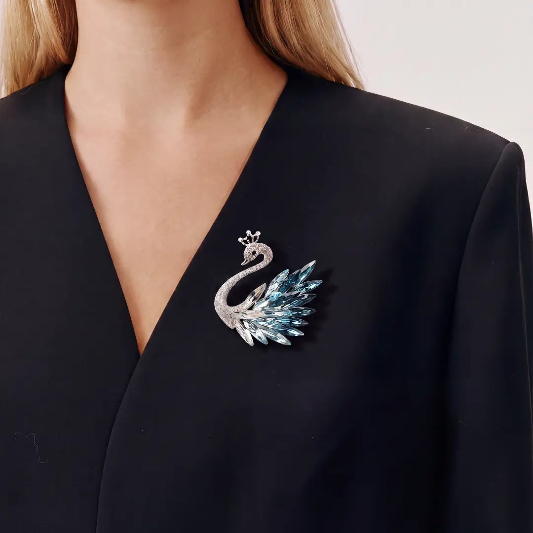 A silver-toned peacock brooch with light blue rhinestones, worn on the chest of a model wearing a black V-neck blazer.