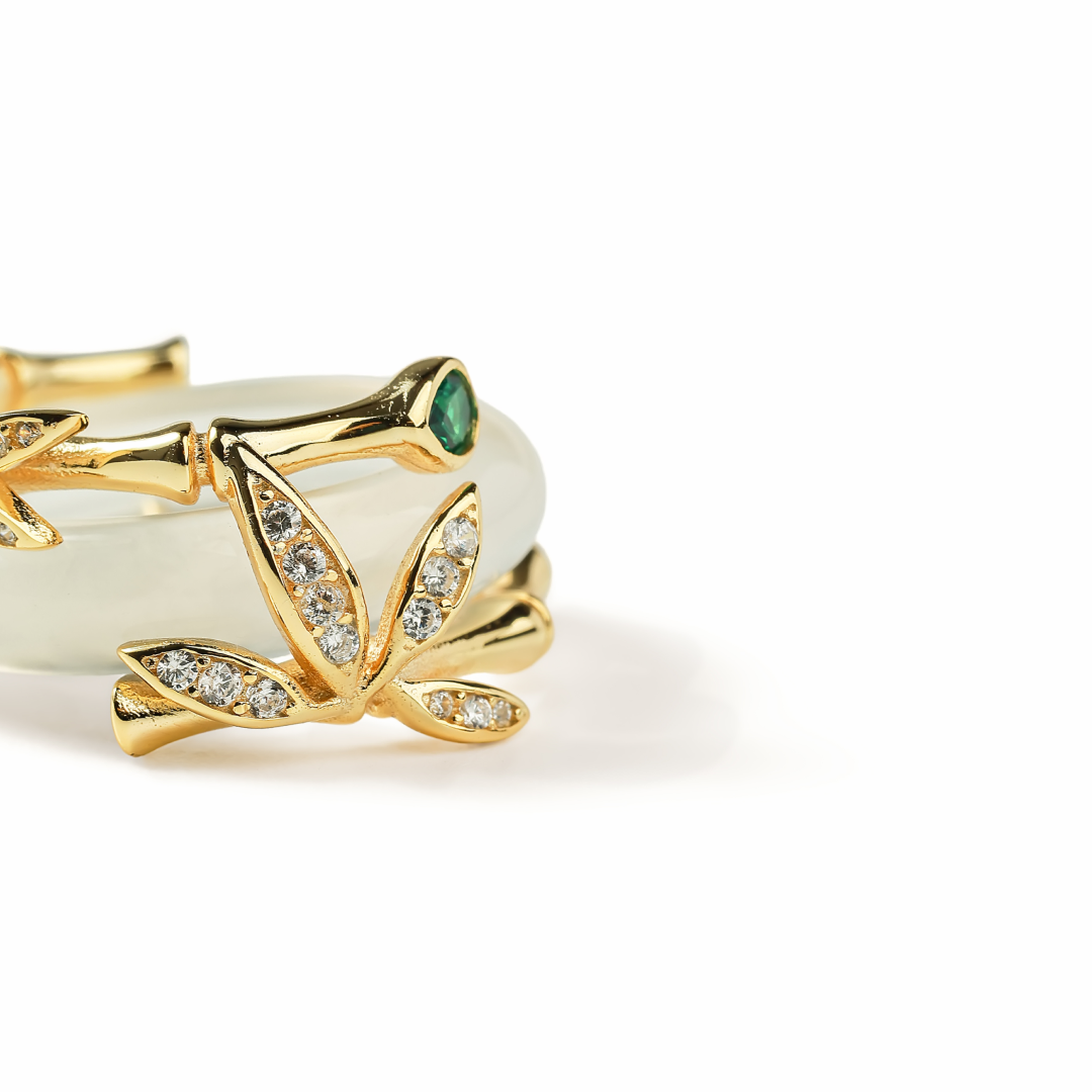 Aiko Tanaka ring close-up, gold bamboo leaves with crystals curling over a white jade band, on a white background