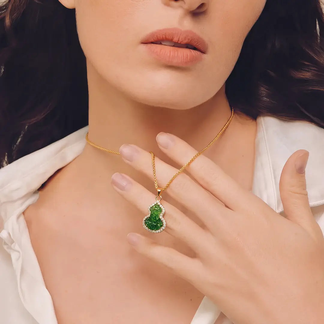 Aiko Tanaka Hisago necklace, a green jade-tone gourd pendant on a gold chain, worn with hand at the collarbone