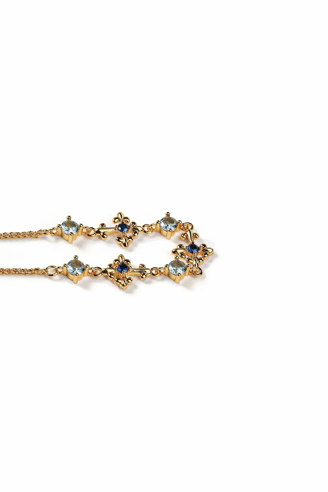 Aiko Tanaka Sazanami bracelet laid flat, a gold chain of small blue and clear crystal flowers, on white