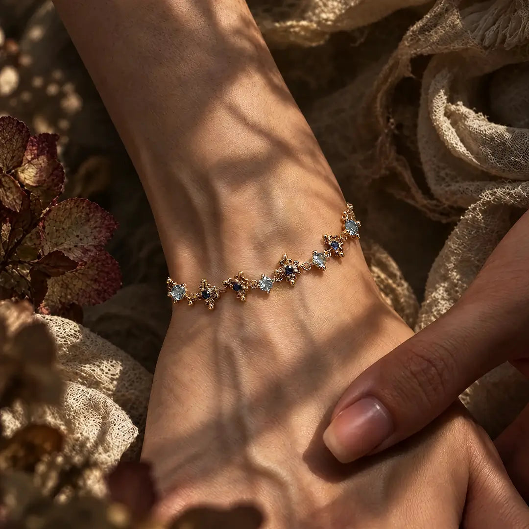 Aiko Tanaka Sazanami bracelet, a gold chain of small blue and clear stone flowers, worn on the wrist in warm light