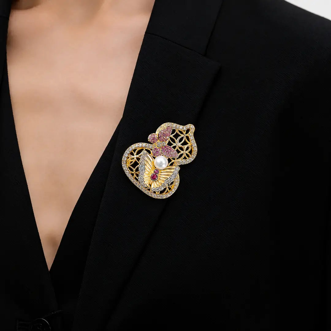 Aiko Tanaka Yugen brooch, a gold filigree gourd with a pink flower, worn on a black V-neck top